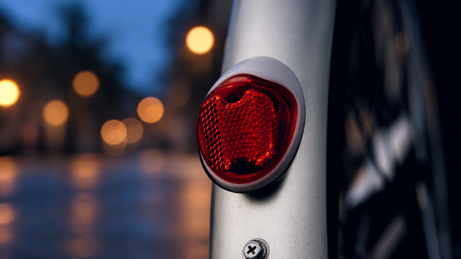 Red rear bicycle reflector mounted on a silver mudguard at dusk