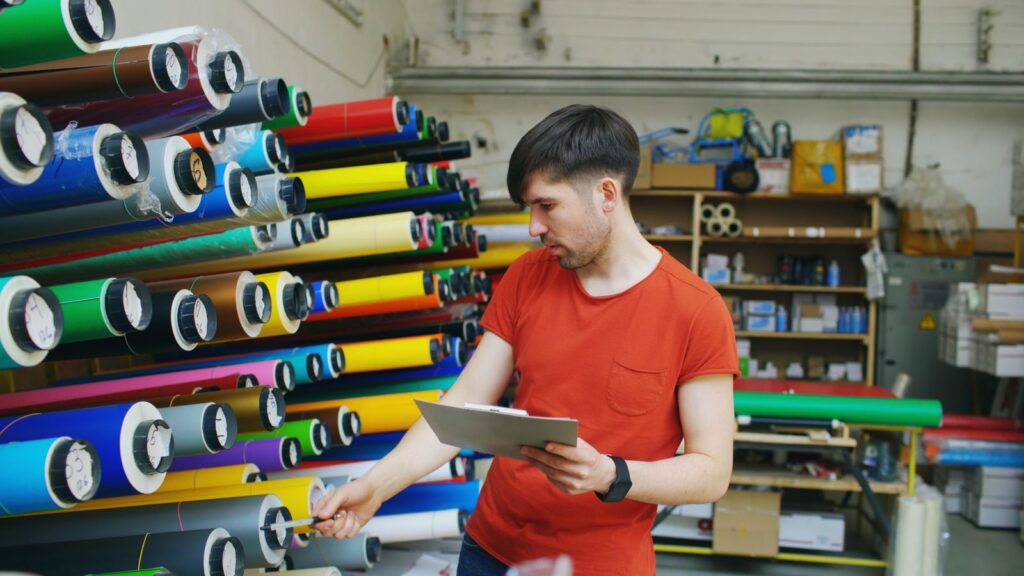Worker checking material rolls against a list in a warehouse
