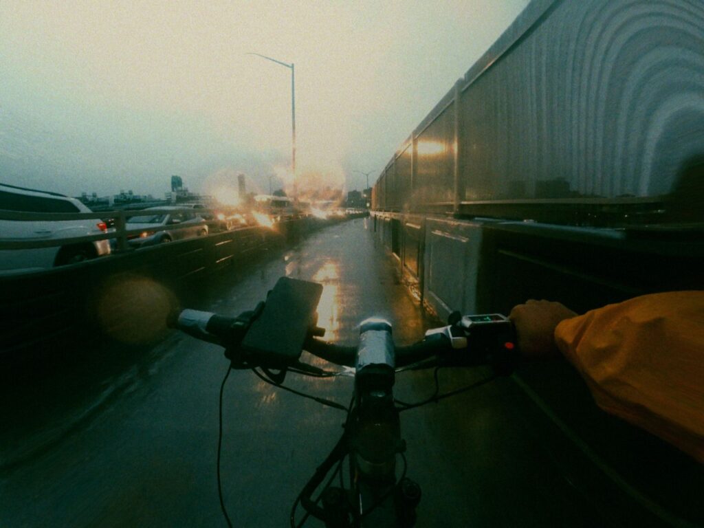 Cyclist in an orange rain jacket riding on a wet road at dusk