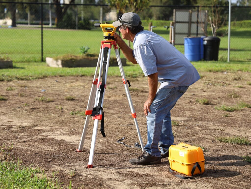 Surveyor looking through an automatic level on a tripod at a cleared site