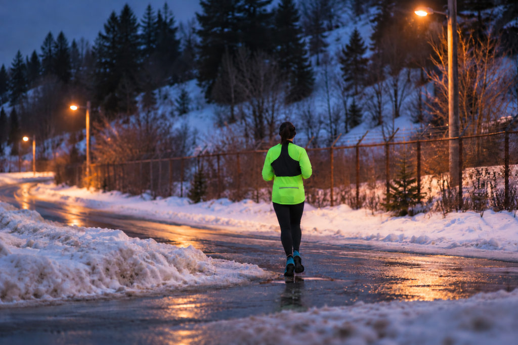 Runner in a fluorescent yellow-green running jacket on a snowy road in the evening