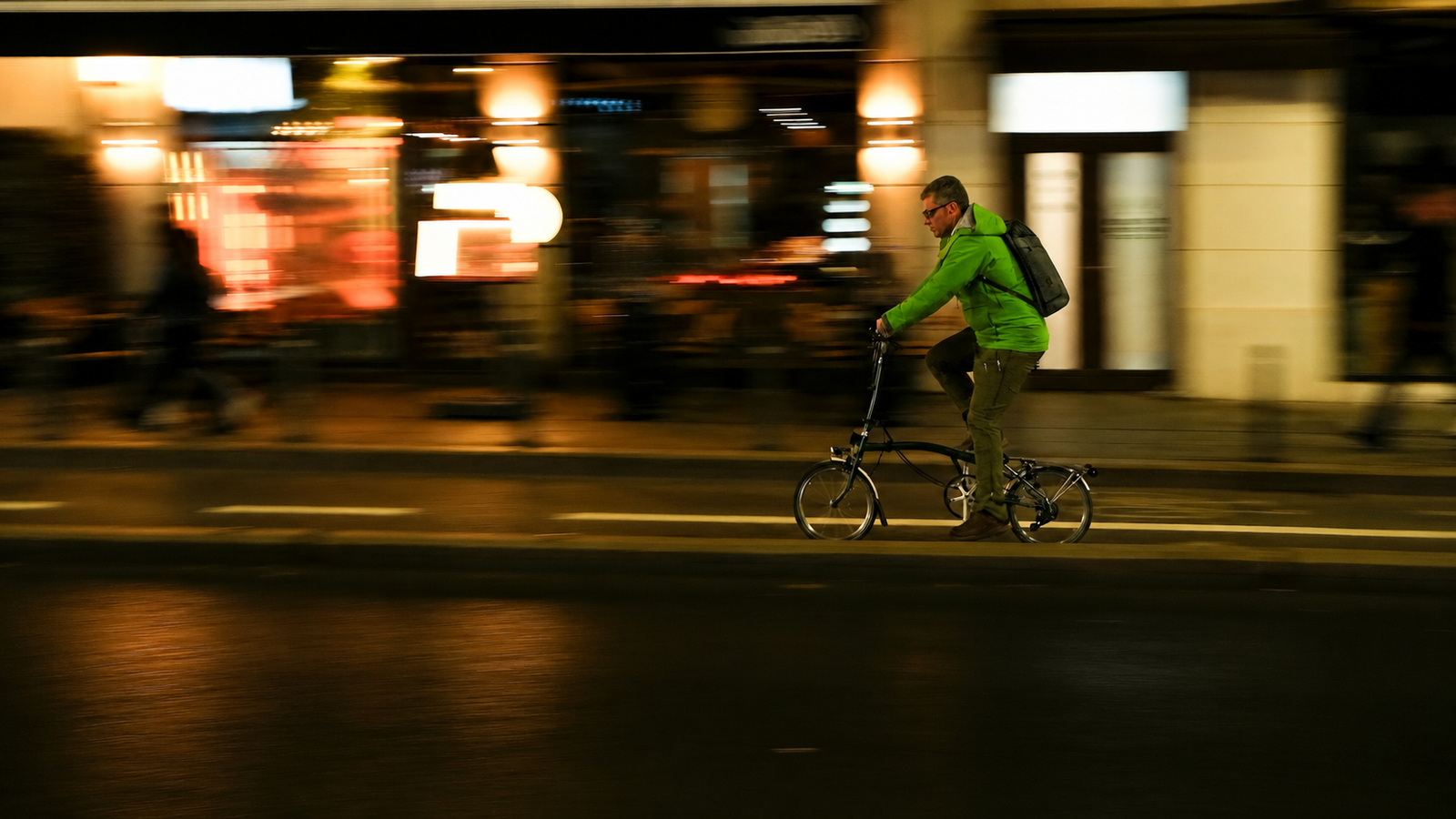 Man in a green jacket commuting by folding bike on a city street at night