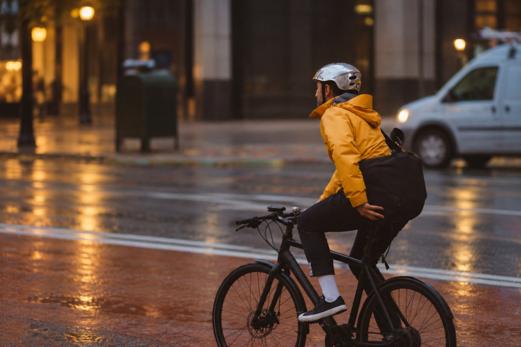 Man in a yellow hooded rain jacket cycling on a wet city street at dusk