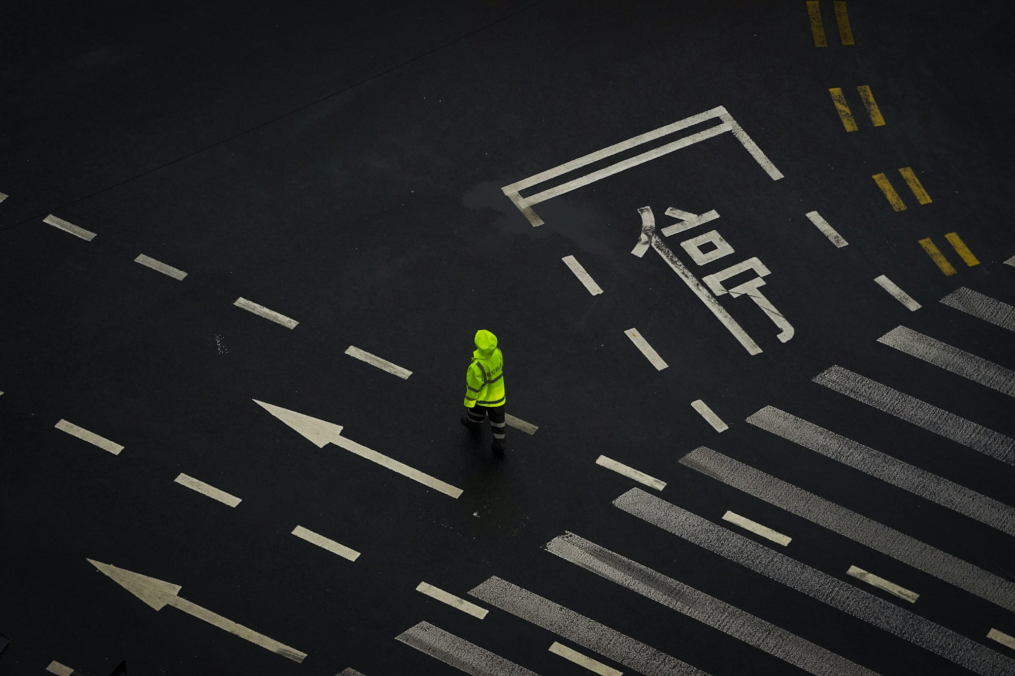 Person in a fluorescent hooded rain jacket with reflective bands crossing a wet street