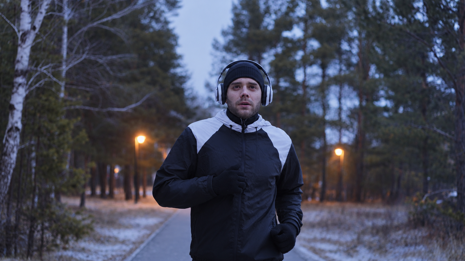 Runner in a black and white running jacket on a park path at winter dusk