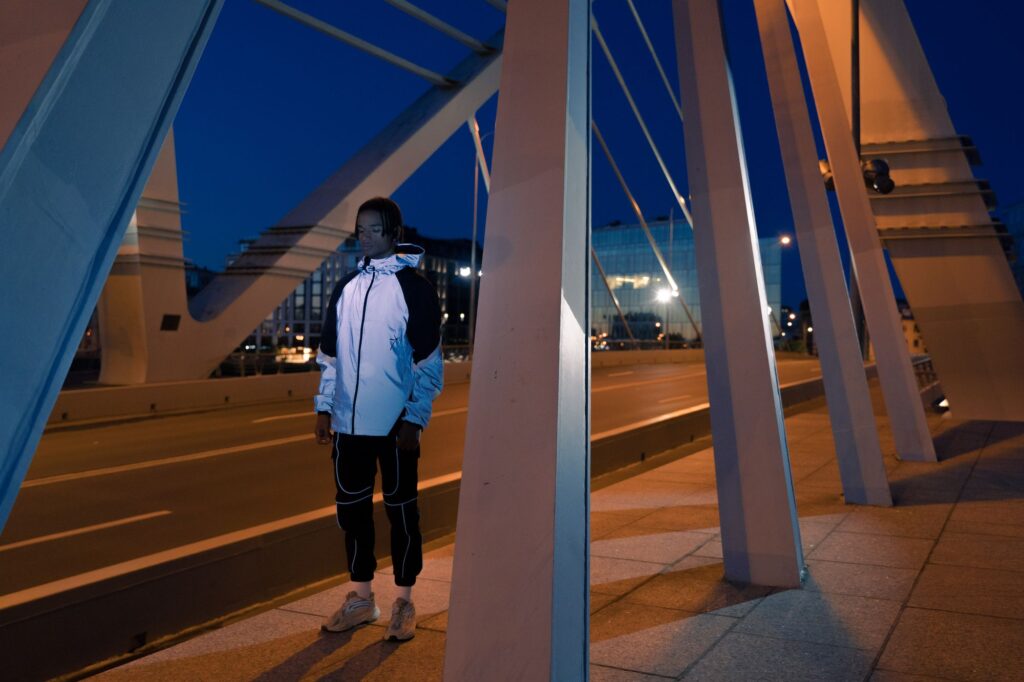 Man in a silver reflective hooded jacket shining on a city bridge at dusk