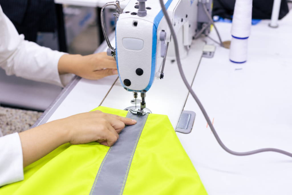 Industrial sewing machine stitching silver reflective tape onto fluorescent yellow fabric