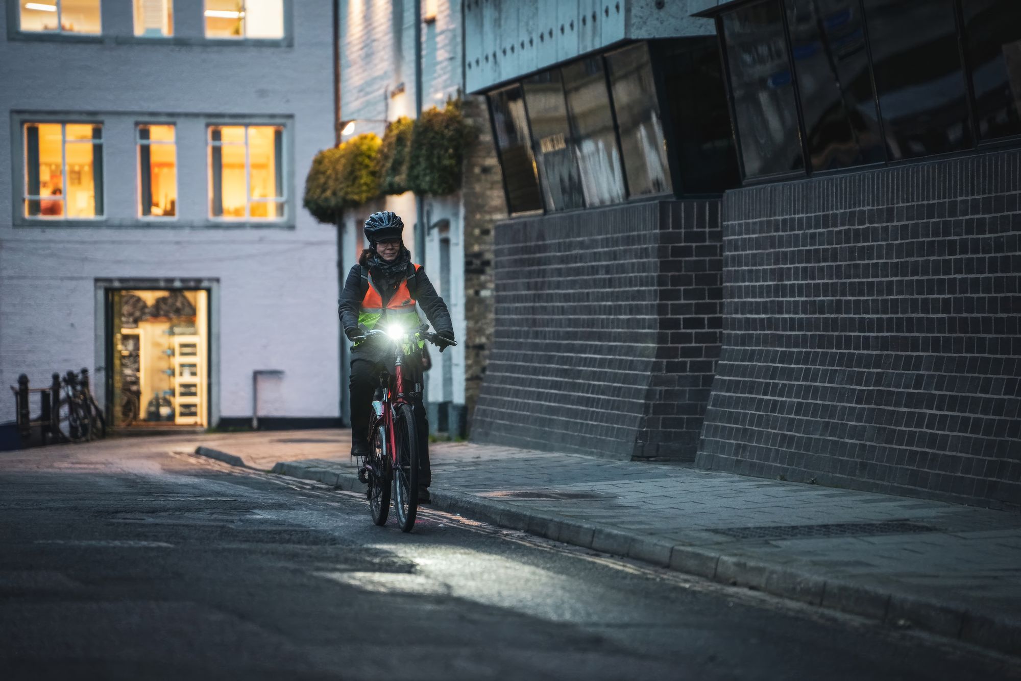 Cyclist in an orange and yellow reflective vest riding with a bright front light at dusk